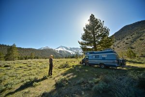 person standing next to a blue RV in nature