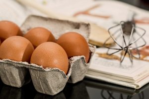 five eggs sitting in a carton next to a whisk