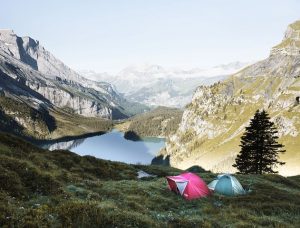 one pink and one blue tent set up next to a lake