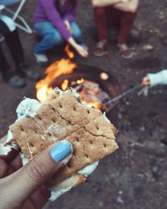 hand holding a s'more in front of a campfire